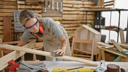 Una mujer enfocada arenas un pedazo de madera en su taller de carpintería, encarnando habilidad y creatividad.