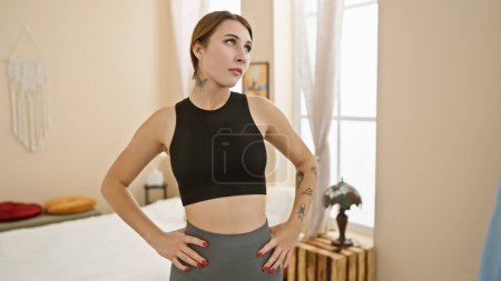 Foto de Una joven confiada posa con las manos en las caderas en un dormitorio elegante, exudando elegancia y una estética moderna. - Imagen libre de derechos