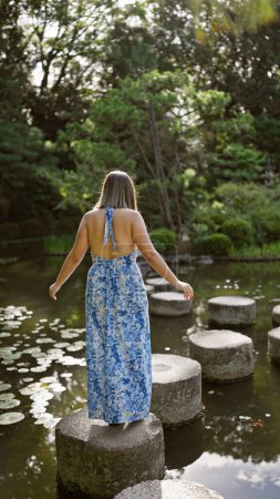 Beautiful hispanic woman's leisurely summer walk along stone path crossing a lake at traditional heian jingu shrine, kyoto