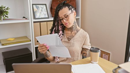 Photo for Hispanic amputee woman boss, a business powerhouse, reading crucial documents on laptop, focused at work in elegant office - Royalty Free Image