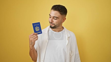Handsome young adult man examines a cuban passport against an isolated yellow background