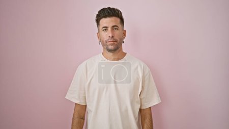 Photo for Cool young hispanic man, a relaxed yet concentrated expression marking his handsome face. he's standing casually to the side, isolated over a pink background, looking seriously into the camera - Royalty Free Image