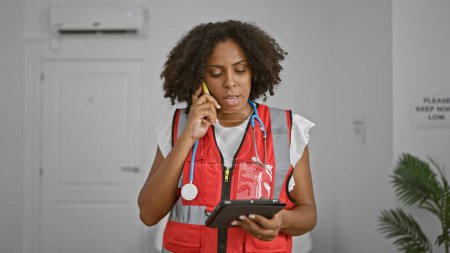 Téléchargez les photos : Infirmière afro-américaine au téléphone dans le corridor de la clinique médicale - en image libre de droit