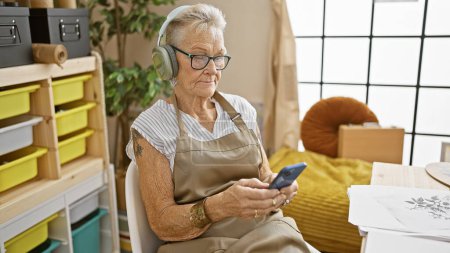 Photo for Senior grey-haired woman artist listening to music at art studio - Royalty Free Image