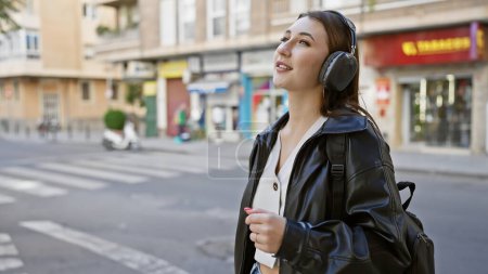 Téléchargez les photos : Une jeune femme aime la musique sur écouteurs tout en marchant dans une rue animée de la ville. - en image libre de droit