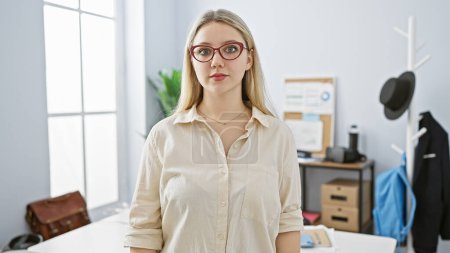 Photo for A professional young woman stands confidently in a modern office setting, exuding competence and approachability. - Royalty Free Image