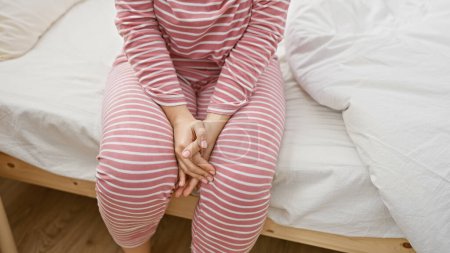 Téléchargez les photos : Une jeune femme en pyjama rayé est assise sur un lit dans une chambre lumineuse et confortable. - en image libre de droit