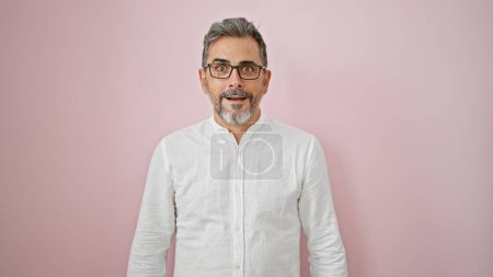 Photo for Oh wow! grey-haired young hispanic man with surprising expression, amazed and standing over an isolated pink background, totally incredible. handsome male with open mouth and glasses. - Royalty Free Image