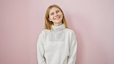 Photo for A cheerful blonde woman with blue eyes wearing a white sweater smiles against a pink background. - Royalty Free Image