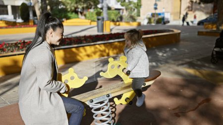 Photo for A young woman and little girl enjoy playful bonding on a seesaw at a sunny outdoor playground, expressing family love. - Royalty Free Image