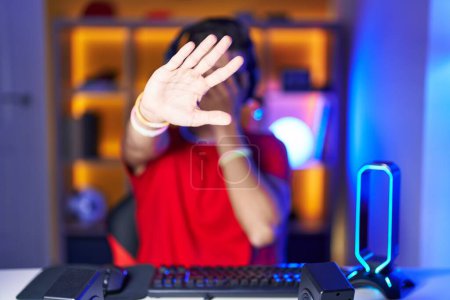 Téléchargez les photos : Jeune homme hispanique jouant à des jeux vidéo couvrant les yeux avec les mains et faisant un geste d'arrêt avec expression triste et peur. concept embarrassé et négatif. - en image libre de droit