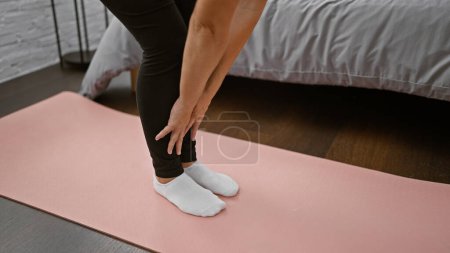 Téléchargez les photos : Femme caucasienne souriante étirant ses jambes dans un exercice de yoga matinal relaxant sur le sol de la chambre, mains soutenant l'équilibre, vêtements de sport posant symbolise le bien-être, méditation calme à l'intérieur. - en image libre de droit
