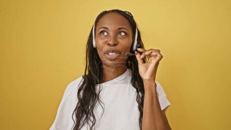 Foto de Mujer afroamericana con auriculares contra fondo amarillo que demuestra profesionalismo en el servicio al cliente. - Imagen libre de derechos