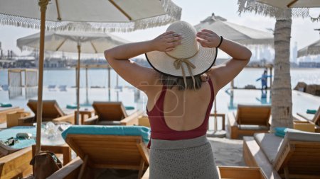 Téléchargez les photos : Une jeune femme profite d'une piscine luxueuse dans une station balnéaire, tenant son chapeau de paille. - en image libre de droit