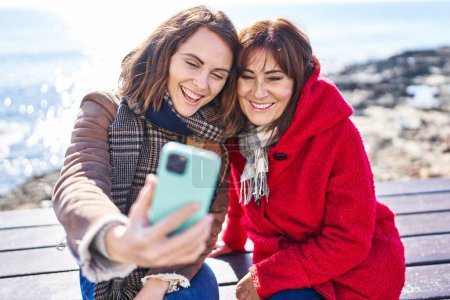 Photo for Two women mother and daughter make selfie by smartphone sitting on bench at seaside - Royalty Free Image