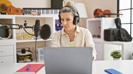 Téléchargez les photos : Jeune journaliste blonde utilisant un ordinateur portable parlant sur l'émission de radio au studio de radio - en image libre de droit