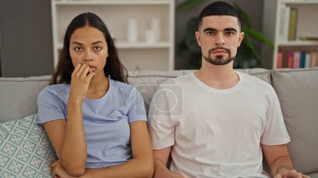 Upset beautiful couple in disagreement, silently looking at each other, sitting on the sofa in their home's living room