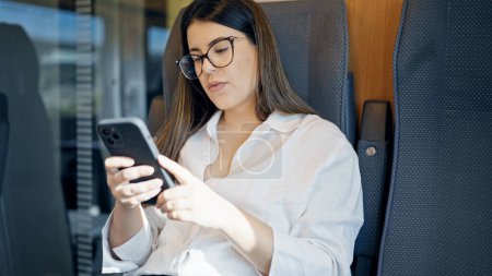 Foto de Mujer hispana hermosa joven usando teléfono inteligente sentado dentro de vagón de tren - Imagen libre de derechos