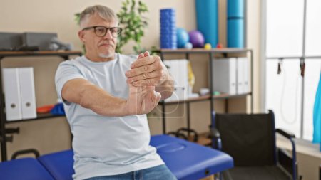 Senior man stretching wrist during physiotherapy in a rehabilitation clinic
