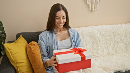 Photo for Exuding joy, confident, young hispanic woman smiling whiles sitting on her comfortable sofa at home, unpacking her surprising birthday gift - Royalty Free Image