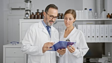 Photo for Serious chemists in lab, two science partners engrossed in reading crucial document on clipboard, immersed in research work together in indoor laboratory - Royalty Free Image