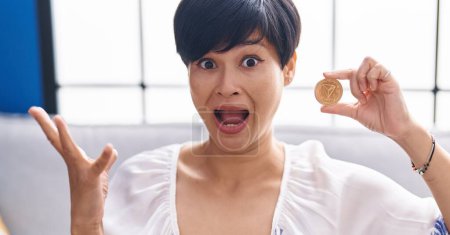 Photo for Young asian woman with short hair holding tron cryptocurrency coin celebrating victory with happy smile and winner expression with raised hands - Royalty Free Image