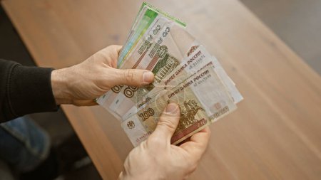 Foto de Primer plano de las manos del hombre contando rublos rusos en interiores, lo que sugiere transacciones financieras o ahorros. - Imagen libre de derechos