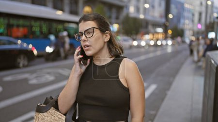 Foto de Hermosa chica latina vestida con gafas, conversando casualmente por teléfono, corriendo para llamar a un taxi en las concurridas calles de Madrid - Imagen libre de derechos