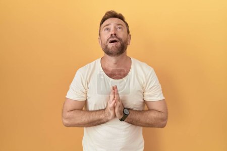 Photo for Middle age man with beard standing over yellow background begging and praying with hands together with hope expression on face very emotional and worried. begging. - Royalty Free Image