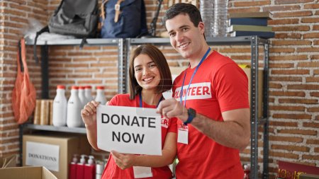Téléchargez les photos : Homme et femme bénévoles debout ensemble tenant du papier avec un don maintenant message au centre de charité - en image libre de droit