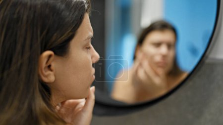 Young beautiful hispanic woman looking for pimples at the mirror in the bathroom