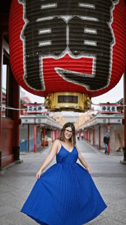 Sprudelnde hispanische Frau tanzt fröhlich und dreht sich in wunderschönem Kleid inmitten der prachtvollen Architektur des Senso-ji Tempels in Tokio. tourt durch Japan, verströmt sie Glück in urbanen Urlaubsabenteuern.
