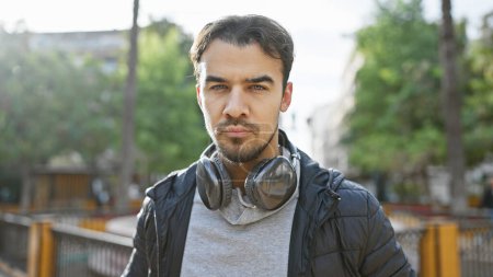 Foto de Guapo joven hispano con barba usando auriculares al aire libre en la naturaleza. - Imagen libre de derechos