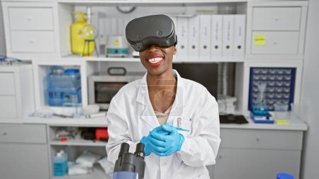 Foto de Científica afroamericana que realiza investigación médica en laboratorio, utilizando gafas de realidad virtual de vanguardia para una videollamada dinámica - Imagen libre de derechos