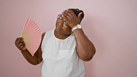 African american woman using handfan suffering for hot over isolated pink background