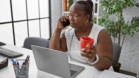 Foto de Jefa afroamericana trenzada, entregándose a su expreso matutino, entablando una conversación seria sobre el trabajo en el teléfono inteligente en su espacio de oficina - Imagen libre de derechos