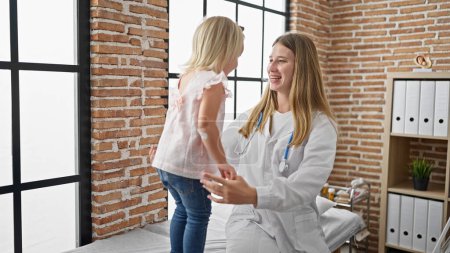 Téléchargez les photos : Médecin pédiatre partage un câlin chaleureux avec un enfant heureux patient à l'intérieur de la clinique, sourire radieux confiant dans les soins de santé - en image libre de droit