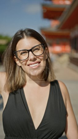 Photo for Confident hispanic woman, beautiful and joyful, cheerfully posing with glasses on, standing and smiling on kyoto's traditional streets, radiating natural and carefree latin expression. - Royalty Free Image