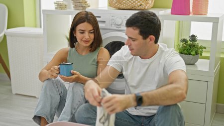 Photo for Beautiful couple smiling confident washing clothes drinking coffee at laundry room - Royalty Free Image