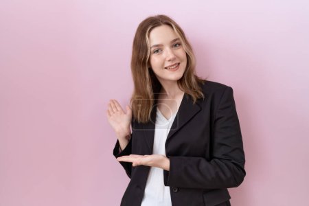 Téléchargez les photos : Jeune femme d'affaires caucasienne veste noire invitant à entrer souriant naturel avec la main ouverte - en image libre de droit