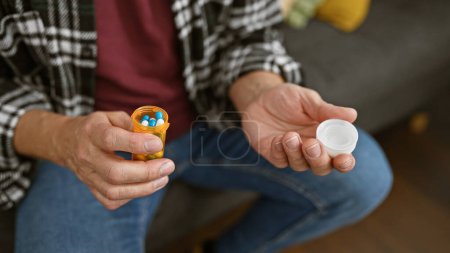 Photo for Middle-aged man holding medication at home, depicting health and domestic life. - Royalty Free Image