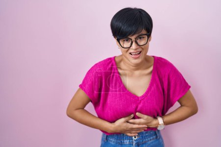 Photo for Young asian woman with short hair standing over pink background smiling and laughing hard out loud because funny crazy joke with hands on body. - Royalty Free Image