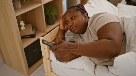 Téléchargez les photos : Africaine américaine regarder la télévision couché sur le lit dans la chambre - en image libre de droit