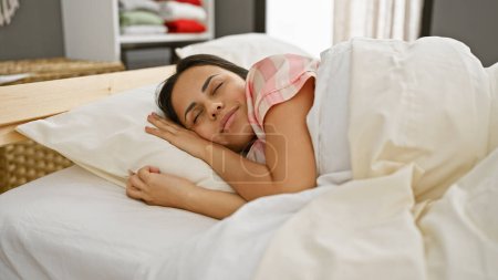 Téléchargez les photos : Une jeune femme hispanique dort paisiblement dans une chambre, mettant en valeur la détente et le confort à la maison. - en image libre de droit