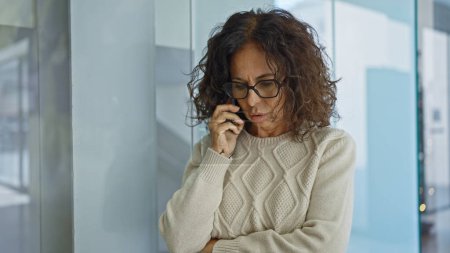 Téléchargez les photos : Femme hispanique mature dans des lunettes parlant au téléphone à l'intérieur au bureau. - en image libre de droit