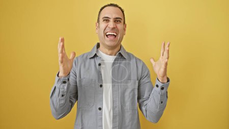 Un alegre hombre hispano haciendo gestos de emoción contra una vibrante pared amarilla, expresando alegría y felicidad.