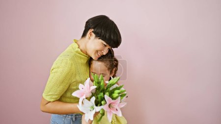 Téléchargez les photos : Câlin mère-fille joyeux avec bouquet souriant sur fond rose isolé, expression de l'amour et du bonheur de la famille - en image libre de droit