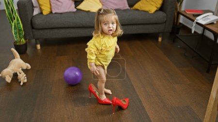 Photo for Cute blonde girl trying on red heels in a cluttered living room, depicting childhood innocence and playfulness at home. - Royalty Free Image