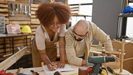 Photo for Two smiling carpenters confidently taking notes in their woodworking workshop - Royalty Free Image