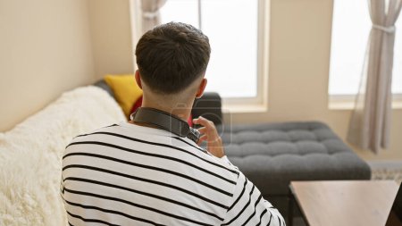 Téléchargez les photos : Jeune homme hispanique portant des écouteurs assis sur le canapé à la maison - en image libre de droit